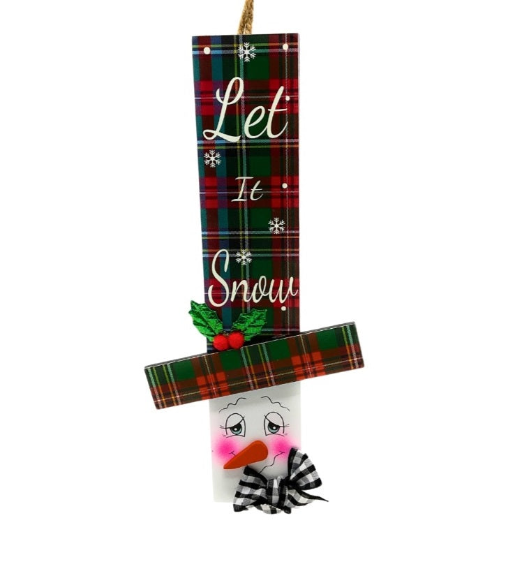 Hanging sign designed to look like a snowman head. One snowman has a red and green buffalo check top hat that reads "Let It Snow." One snowman has a red and green plaid top hat that reads "Come in from the Cold." One snowman has a red and white plaid top hat that reads "There's Snow place like Home."