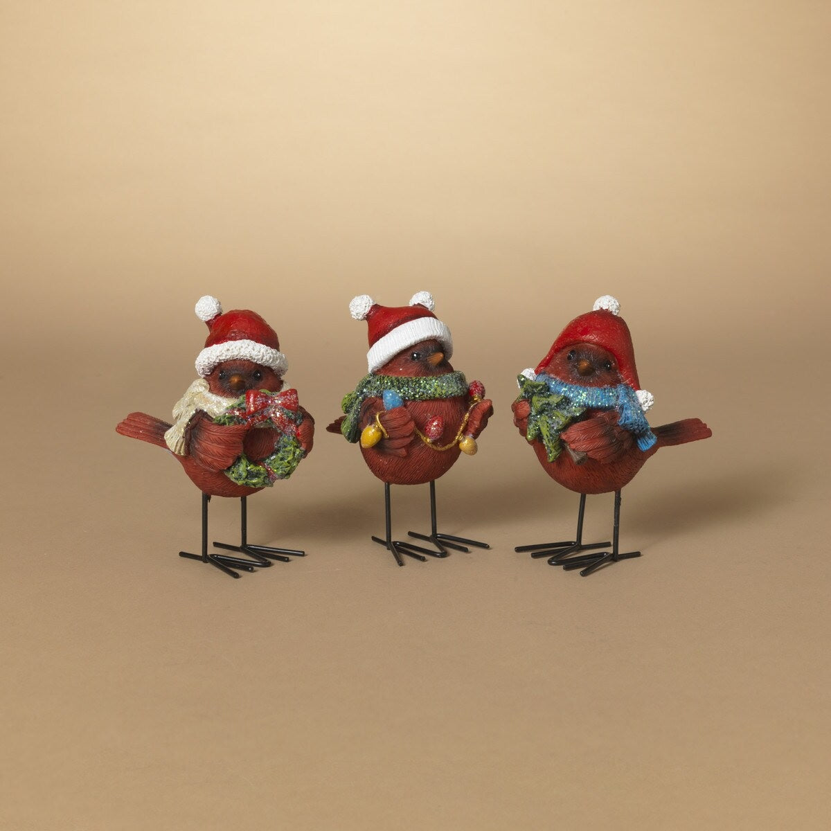 Standing red cardinal decoration for Christmas. One cardinal is wearing a white scarf and holding a wreath. One cardinal is wearing a green scarf and holding a string of lights. One cardinal is wearing a blue scarf and holding a small tree.