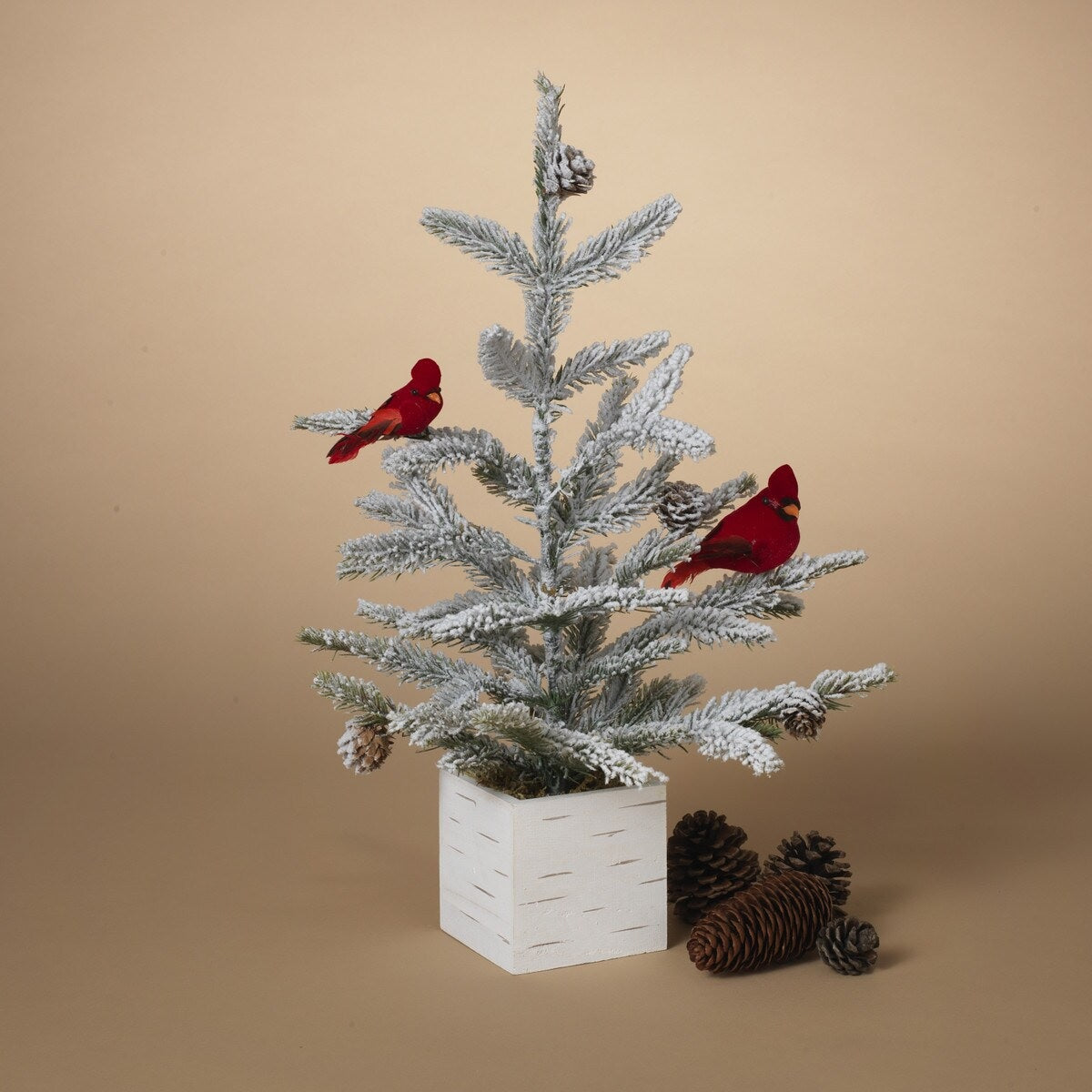 Tabletop tree in a birch planter box. The branches of the tree are dusted with white to mimic snow. The tree is accented with two red cardinal birds and some snow-covered pine cones.