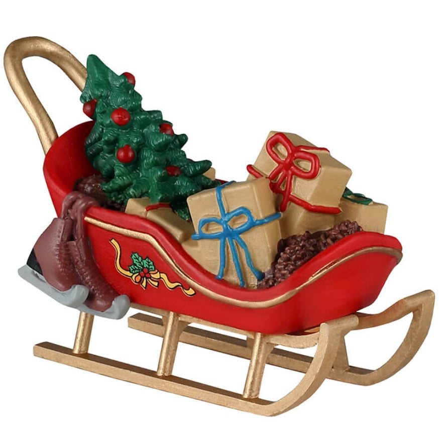 Resin village accessory for a Christmas Lemax tabletop display. Designed to look like a red and gold sled carrying a small, decorated tree, a bunch of presents, pine cones and ice skates.