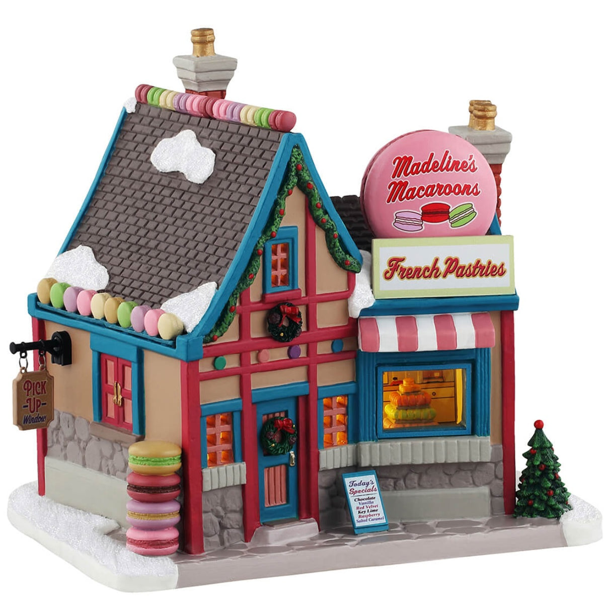 Porcelain lighted building for a Lemax display. Designed to look like a charming, little shop called Madeline's Macaroons French Pastries. Inside the window, you can see a display of macaroons. There are decorated wreaths, garland and a Christmas tree. There's snow on the ground and on the roof. There are also candy accents on the roof and macaroons on the sidewalk.