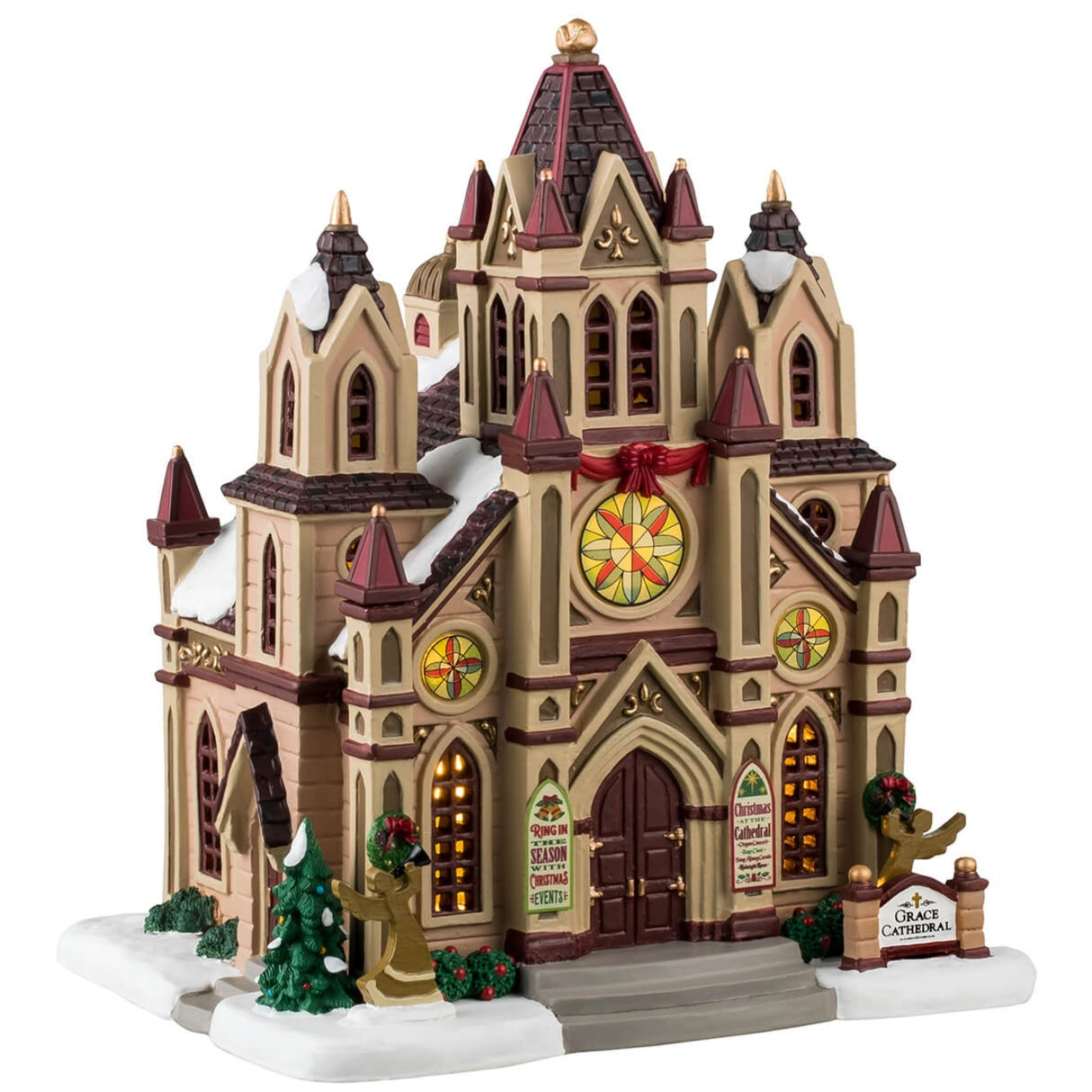 Porcelain lighted building for a Christmas Lemax Village. Designed to look like a giant cathedral. It has maroon, brown, tan and gold accents. There are three circular stained glass windows consisting of yellow, light green and orange colors. There's snow on the roof and the sidewalk. There are decorated trees, wreaths and bushes, as well as two angel silhouette decorations.