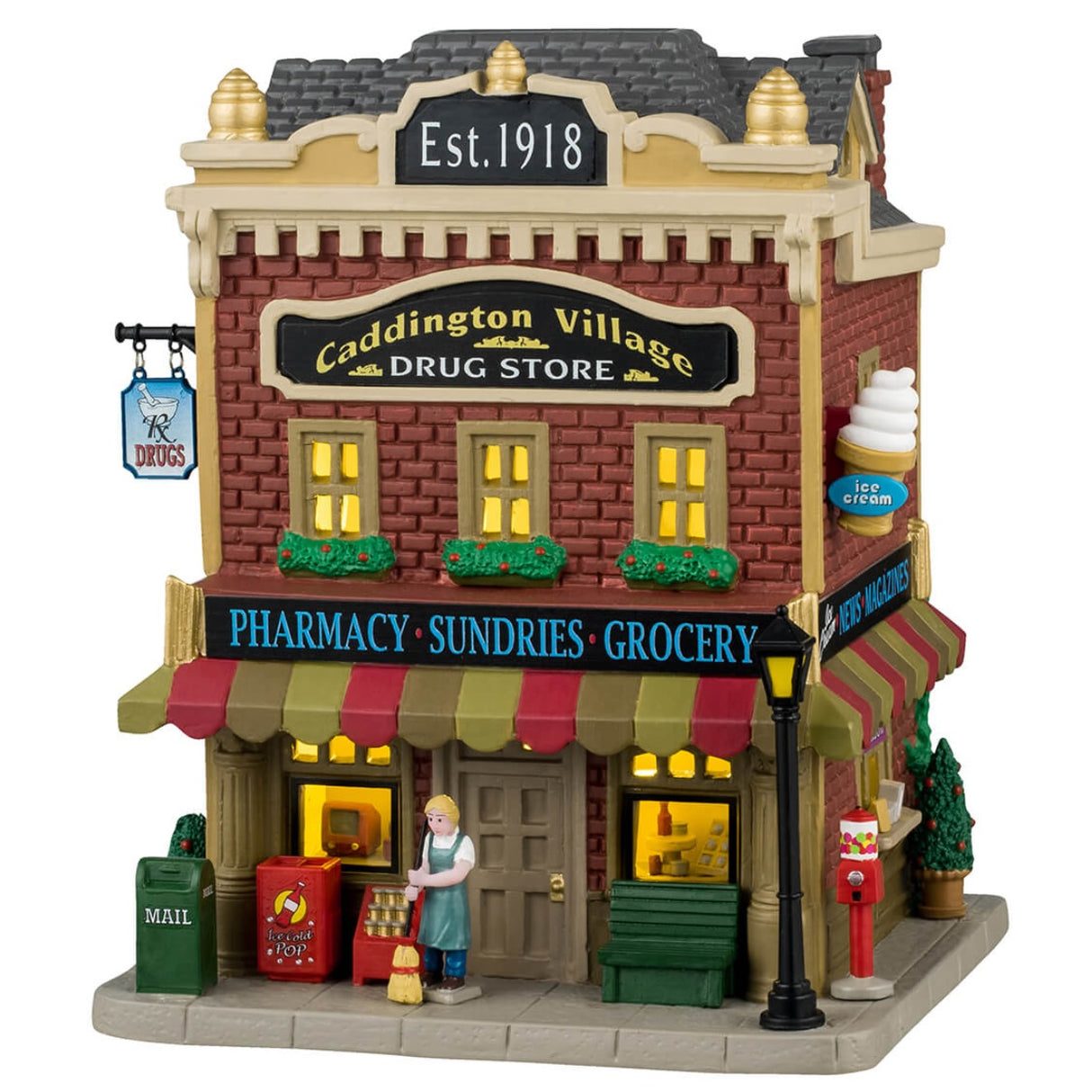 Porcelain lighted building for a Lemax display. Designed to look like a Village Drug Store. Established 1918, there's a pharmacy, sundries, groceries and ice cream. There's a mail box, a cooler with pop, a bench, a gumball machine and potted trees on the sidewalk.
