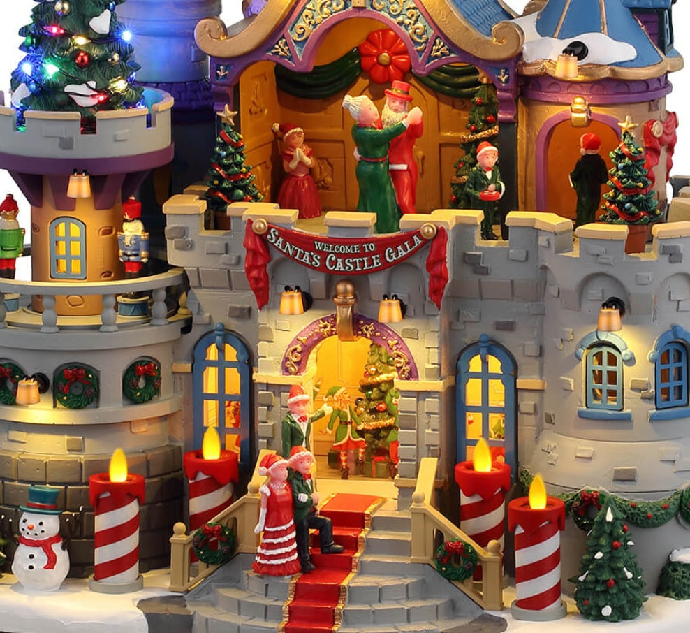Resin lighted building for a Lemax display. Designed to look like a stone castle decorated for a Christmas gala with Santa. There are people dancing on the balcony and decorative nutcrackers. There are decorated Christmas trees, a snowman and red/white striped candle lights outside.