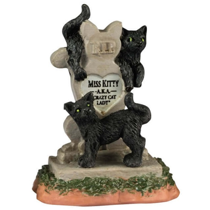 Resin village accents for a Lemax display. Designed to look like three headstones. One has a bat statue on it and it reads "Vlad Vampyr 1452-?" The next one is shaped like a cat and reads "RIP Miss Kitty aka Crazy Cat Lady." There are black cats on it. The next one features a skull with snakes coming out of it and a bunch of red candles lit at the base.
