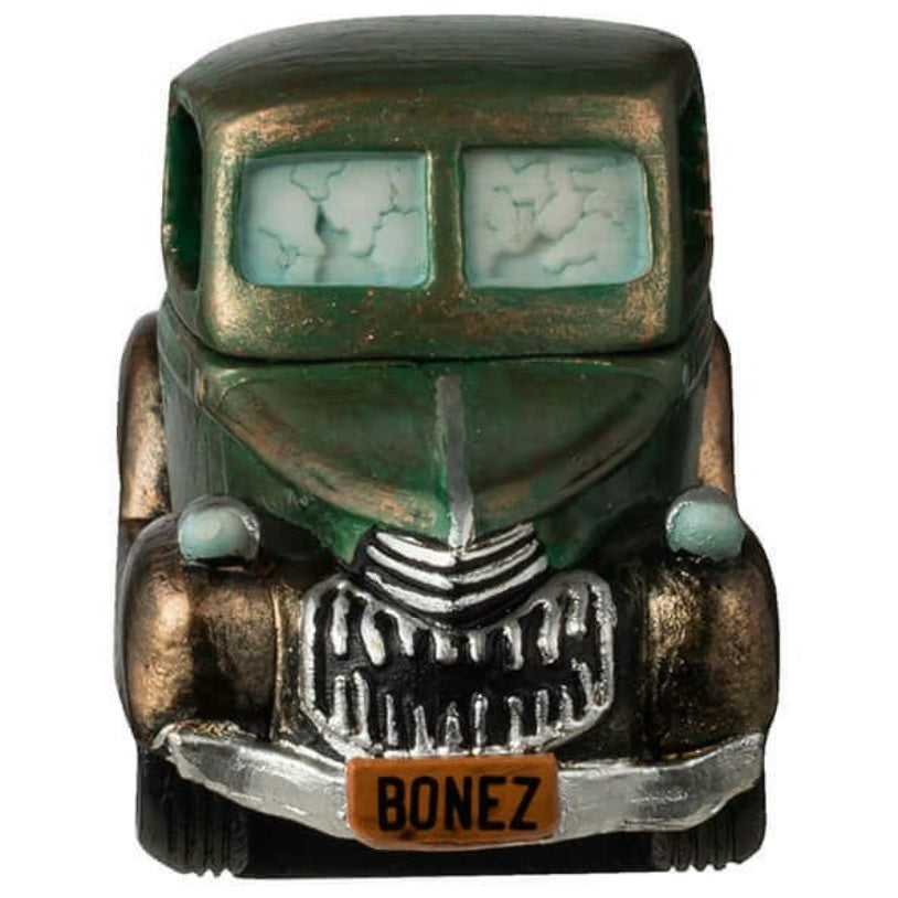 Resin figurine for a Lemax display. Designed to look like a rusty, green truck driven by a skeleton. There's a lot of garbage in the truck bed. The license plate is orange and reads "BONEZ."