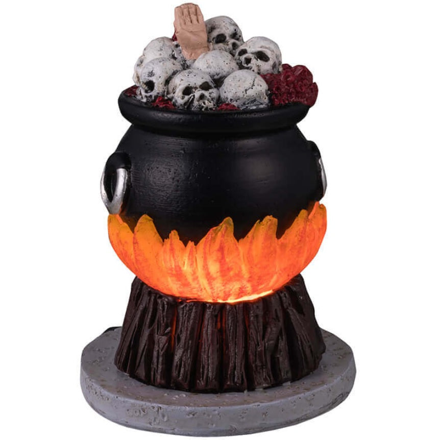 Plastic village accent for a Spooky Town Lemax display. Designed to look like a cauldron over a fire. There are skulls and a hand boiling inside.