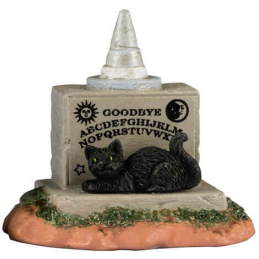 Resin village accents for a Lemax display. Designed to look like three tombstones. One is shaped like a shark and reads "Captain Jack 1957-1978." One is shaped like a pumpkin and reads "Ichabod Crane 1730-1789. Lost his head." The other is shaped like a Ouija board with a witch hat on top and has a black cat sitting on it.