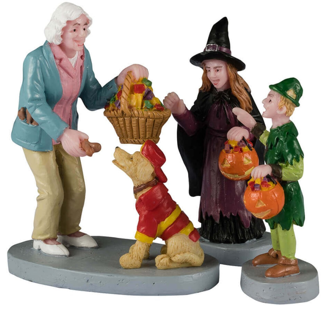 Resin figurines for a Lemax display. Designed to look like an older woman handing out candy to two trick or treaters and a dog. One trick or treater is dressed as a witch. The other is dressed like Peter Pan. The dog is dressed like a firefighter.