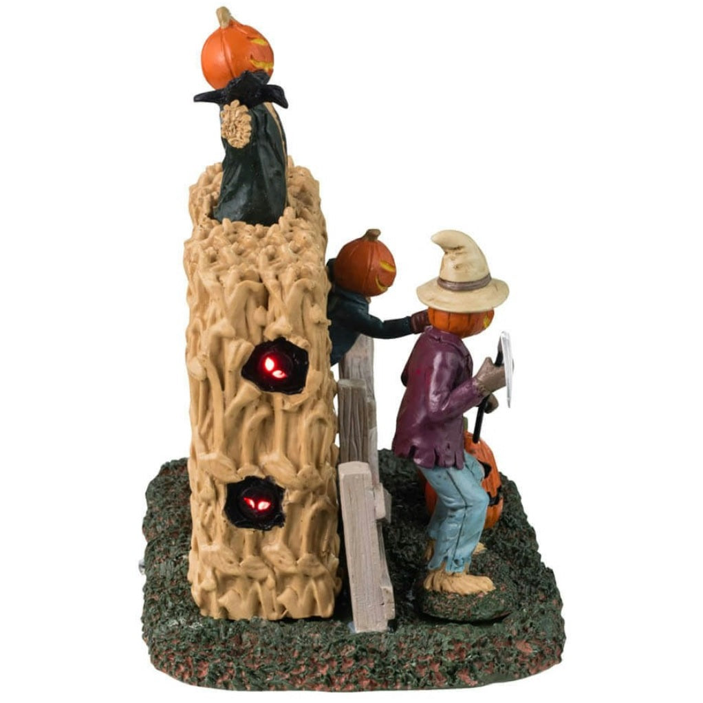 Plastic village accent for a Lemax Spooky Town display. Designed to look like three scarecrows with jack-o-lantern heads coming out of a cornfield. There are glowing red eyes and pumpkins.