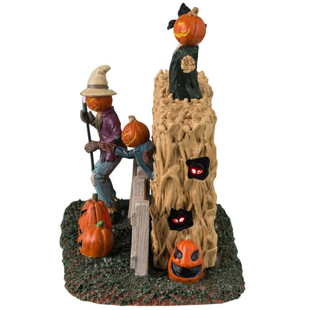Plastic village accent for a Lemax Spooky Town display. Designed to look like three scarecrows with jack-o-lantern heads coming out of a cornfield. There are glowing red eyes and pumpkins.