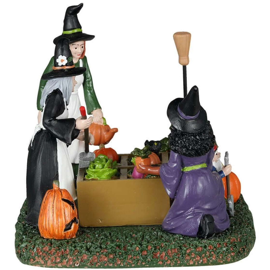 Resin table piece for Lemax display. Designed to look like three witches tending to a garden. There are pumpkins and radishes and lettuce and mushrooms and a black cat surveying the plants. There's a gnome statue holding a shovel.