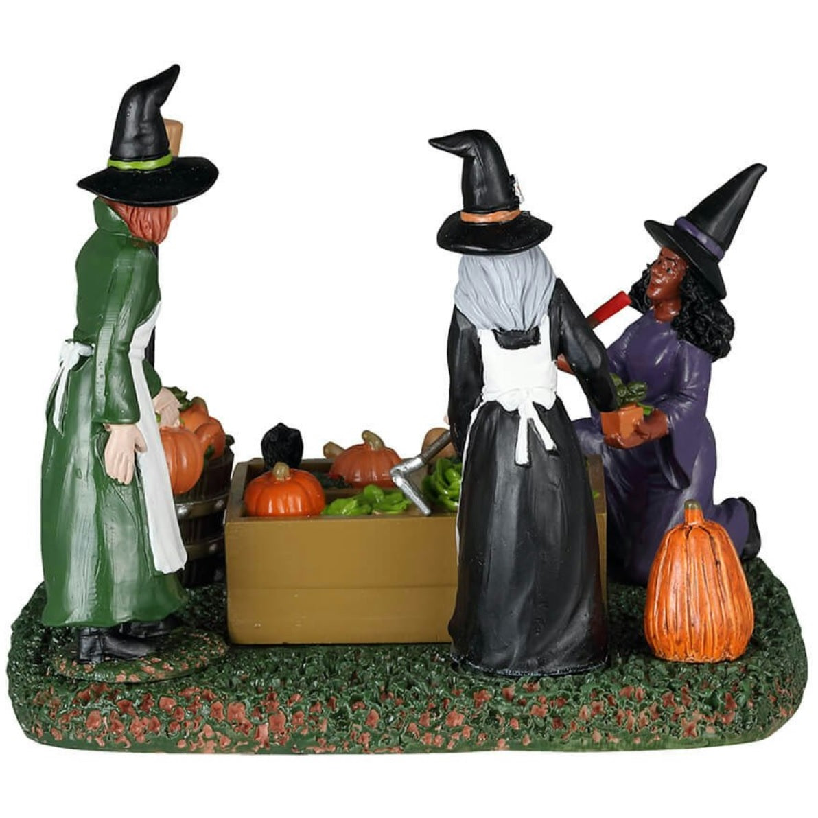 Resin table piece for Lemax display. Designed to look like three witches tending to a garden. There are pumpkins and radishes and lettuce and mushrooms and a black cat surveying the plants. There's a gnome statue holding a shovel.