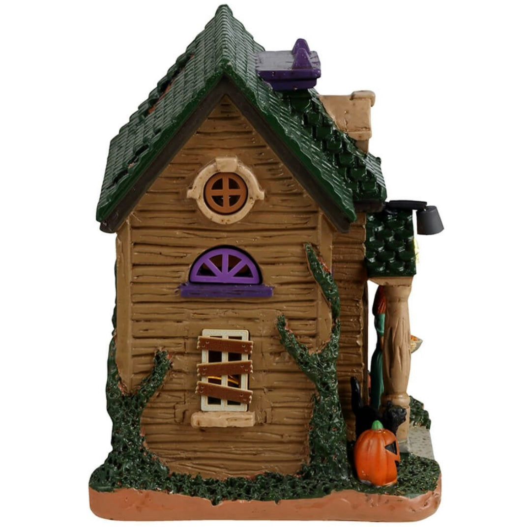 Resin building for a Lemax display. Designed to look like a rundown house. Part of the roof is missing and the windows are boarded up. There's a woman wearing a light blue dress in the doorway handing out candy. There's a black cat and two carved pumpkins and a tombstone that reads RIP.