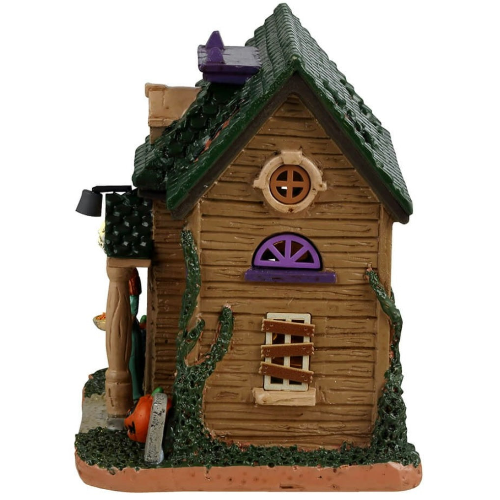 Resin building for a Lemax display. Designed to look like a rundown house. Part of the roof is missing and the windows are boarded up. There's a woman wearing a light blue dress in the doorway handing out candy. There's a black cat and two carved pumpkins and a tombstone that reads RIP.