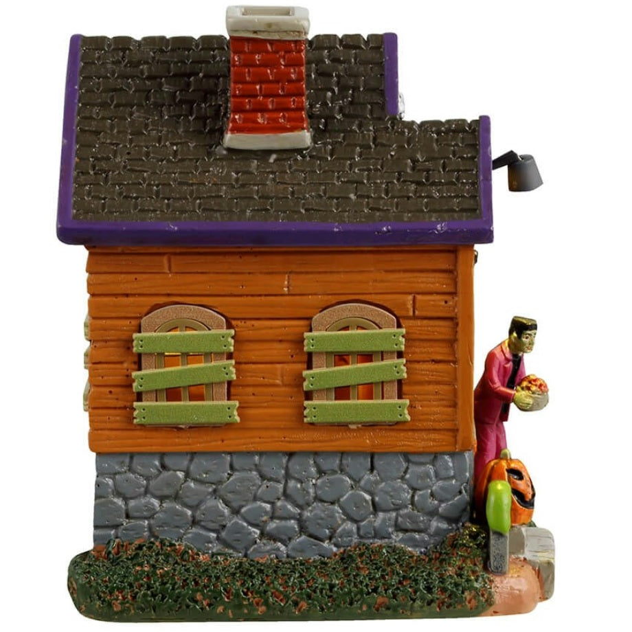 Resin building for a Lemax display. Designed to look like an orange, rundown cabin with boarded up windows and spiders everywhere. Frankenstein is standing on the porch. There are tombstones and carved pumpkins on the front lawn.