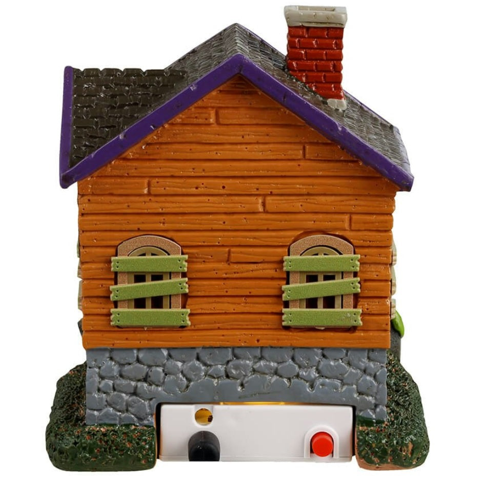 Resin building for a Lemax display. Designed to look like an orange, rundown cabin with boarded up windows and spiders everywhere. Frankenstein is standing on the porch. There are tombstones and carved pumpkins on the front lawn.