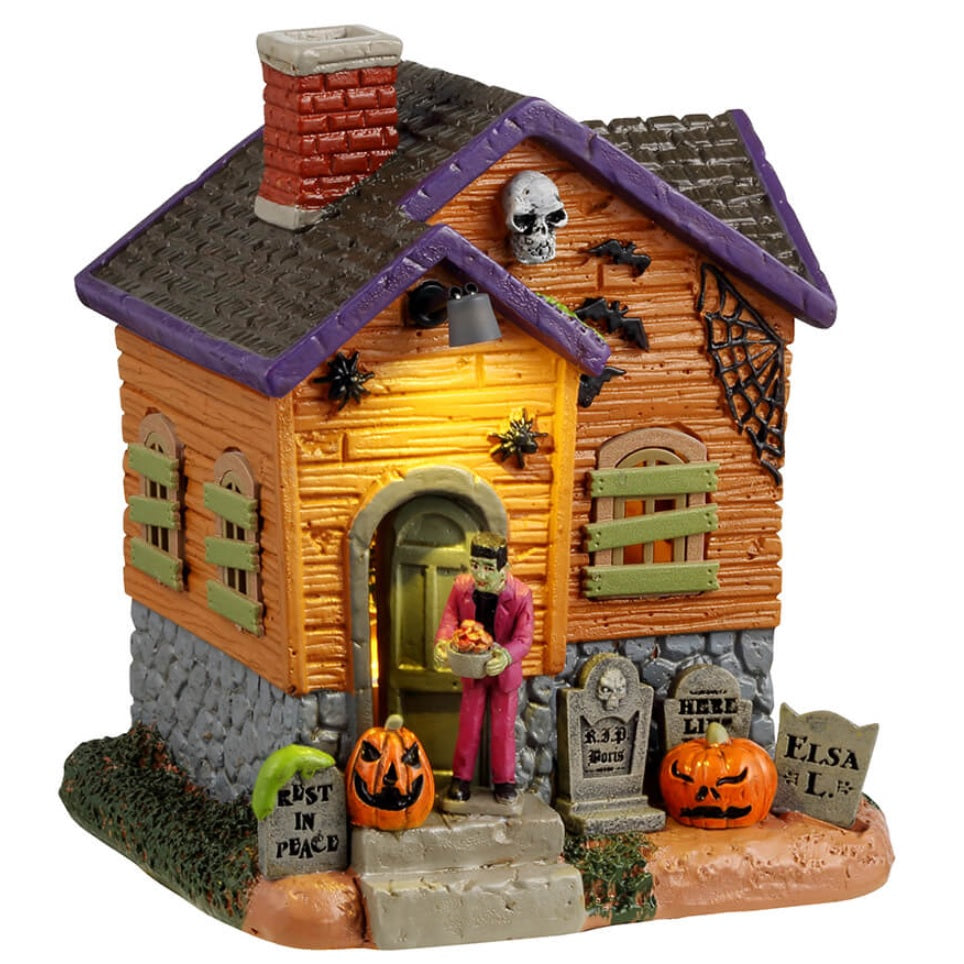 Resin building for a Lemax display. Designed to look like an orange, rundown cabin with boarded up windows and spiders everywhere. Frankenstein is standing on the porch. There are tombstones and carved pumpkins on the front lawn.