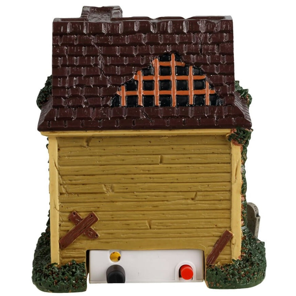 Resin building for a Lemax display. Designed to look like a run down house with moss growing on the side. Part of the roof is missing. There's a black cat on the roof and spiders. There's a skeleton wearing a lime green suit and cape handing out candy. There are tombstones in front of the house and a carved jack-o-lantern.