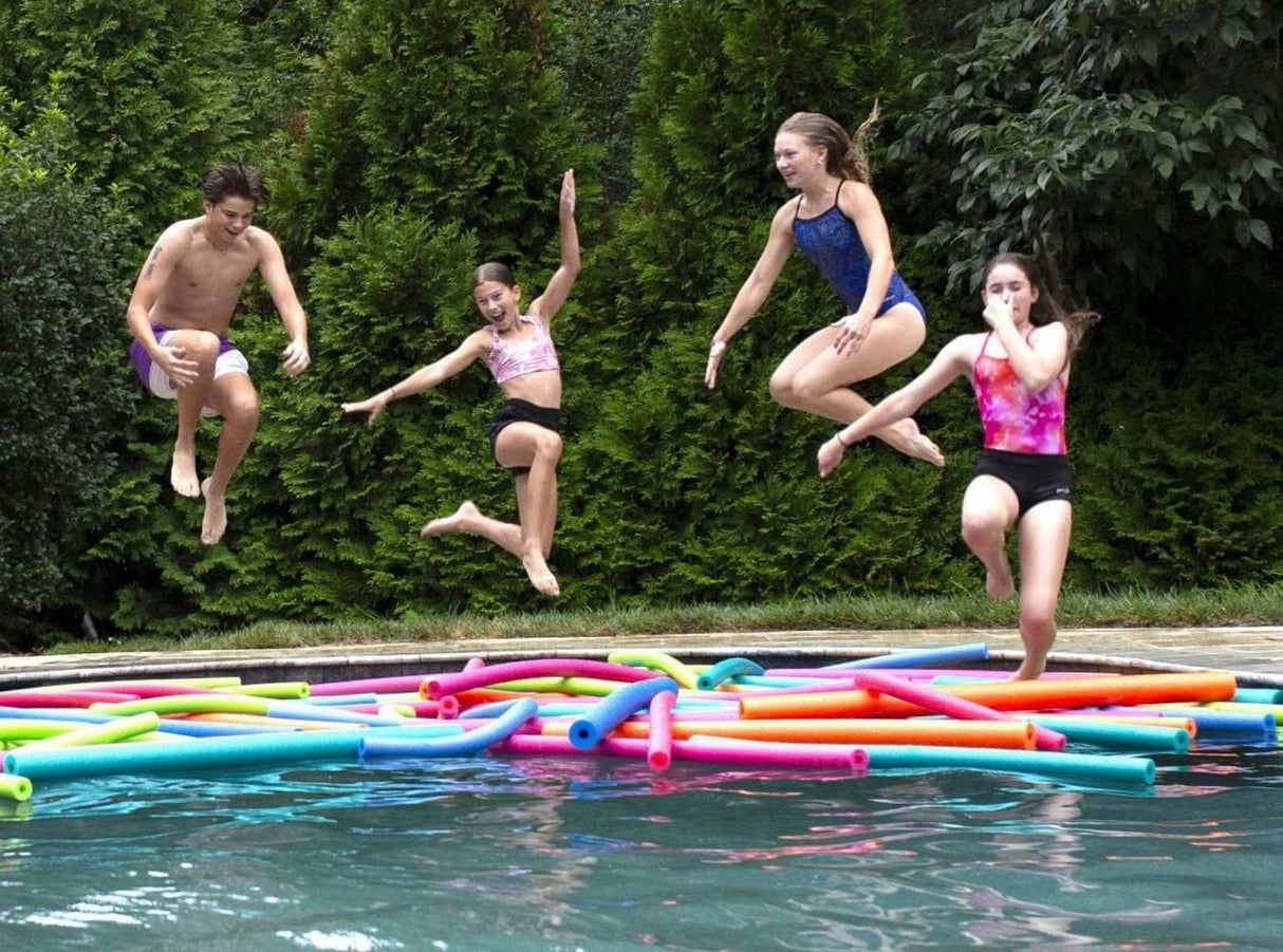 This is a lifestyle image showing four teenagers jumping into a pool filled with different colored pool noodles.