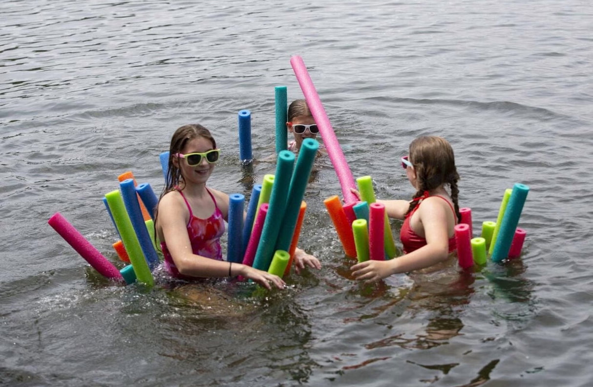 This is a lifestyle image showing three girls riding a bunch of different pool noodles in a lake.