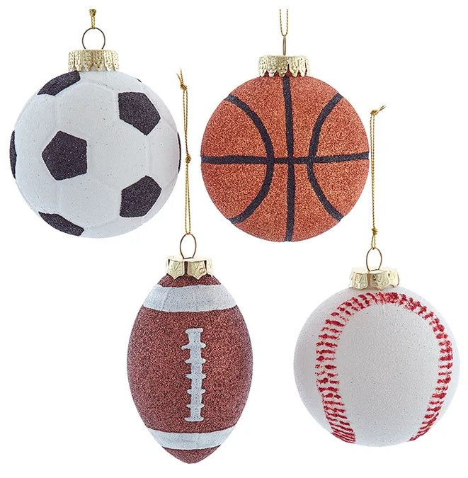 Ornament shaped like a sports ball. There are four different options, each covered in glitter. One is shaped like a soccer ball in black and white glitter. One is shaped like a basketball with orange and black glitter. One is shaped like a football in brown and white glitter. One is shaped like a baseball in white and red glitter.