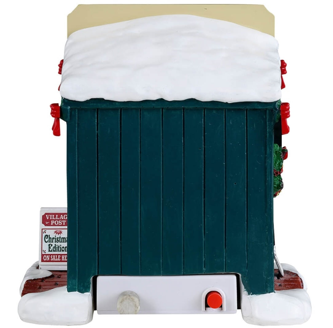 Resin village accent for a Lemax display. Designed to look like a newspaper stand decorated for Christmas. The vendor inside is wearing a winter hat, scarf and coat and is drinking from a white cup.
