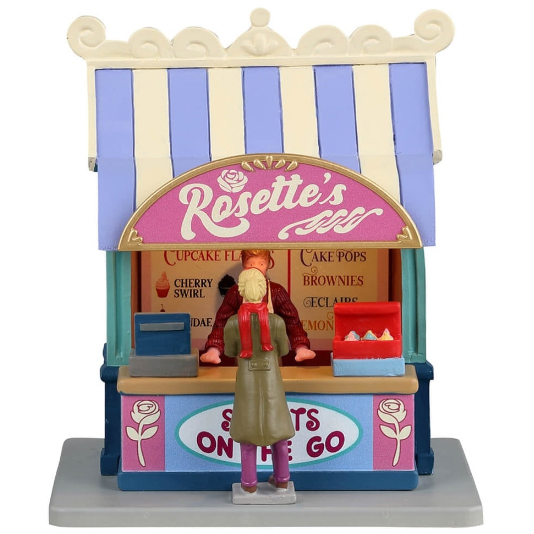 Resin village accent for a Lemax display. Designed to look like a cupcake vendor booth. It's run by Rosette and it's sweets to go. The colors of the booth are light purple, tan, pink, light blue and dark blue.