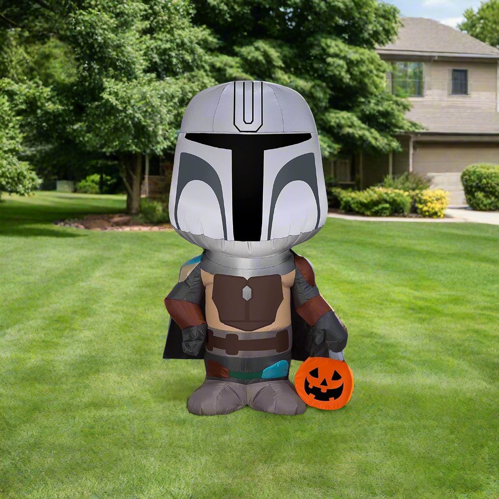 Halloween inflatable shaped like The Mandalorian from the Star Wars universe. He's holding a treat tote bag that looks like a carved pumpkin.