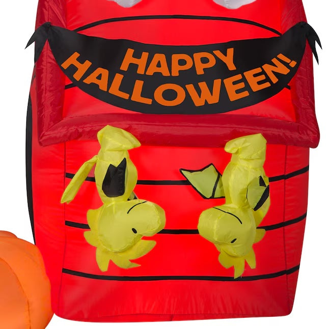 Halloween inflatable shaped like Snoopy the Peanuts cartoon character dressed as a witch and sitting on his red dog house. There are two Woodstock Peanuts cartoon characters hanging from the house like they're bats and there's a pumpkin off to the side.