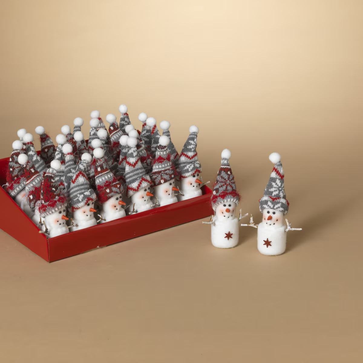 Marshmallow snowman ornament. One snowman is wearing a red knitted hat. One snowman is wearing a gray knitted hat. Both feature details like smiling faces with rosy cheeks, twig arms and snowflake charms.