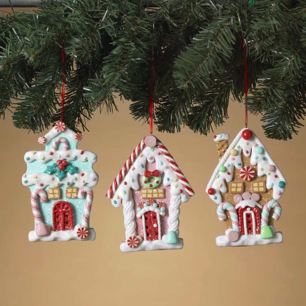 One gingerbread house is teal with a holly leaf accent. One gingerbread house is pink with a wreath accent. One gingerbread house is brown with a peppermint accent. Each ornament features faux candy canes, frosting and gum drop accents.
