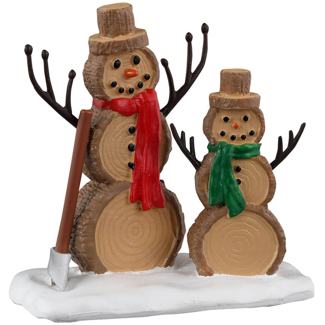 Resin village accessory for a Lemax display. Designed to look like two snowmen made out of wood. There's an axe on the ground next to them. One snowman is wearing a red scarf and the other is wearing a green scarf.