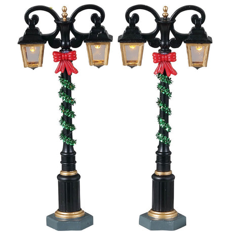 Plastic village accessories for a Lemax display. Designed to look like two regal lampposts wrapped with green tinsel and red bows.