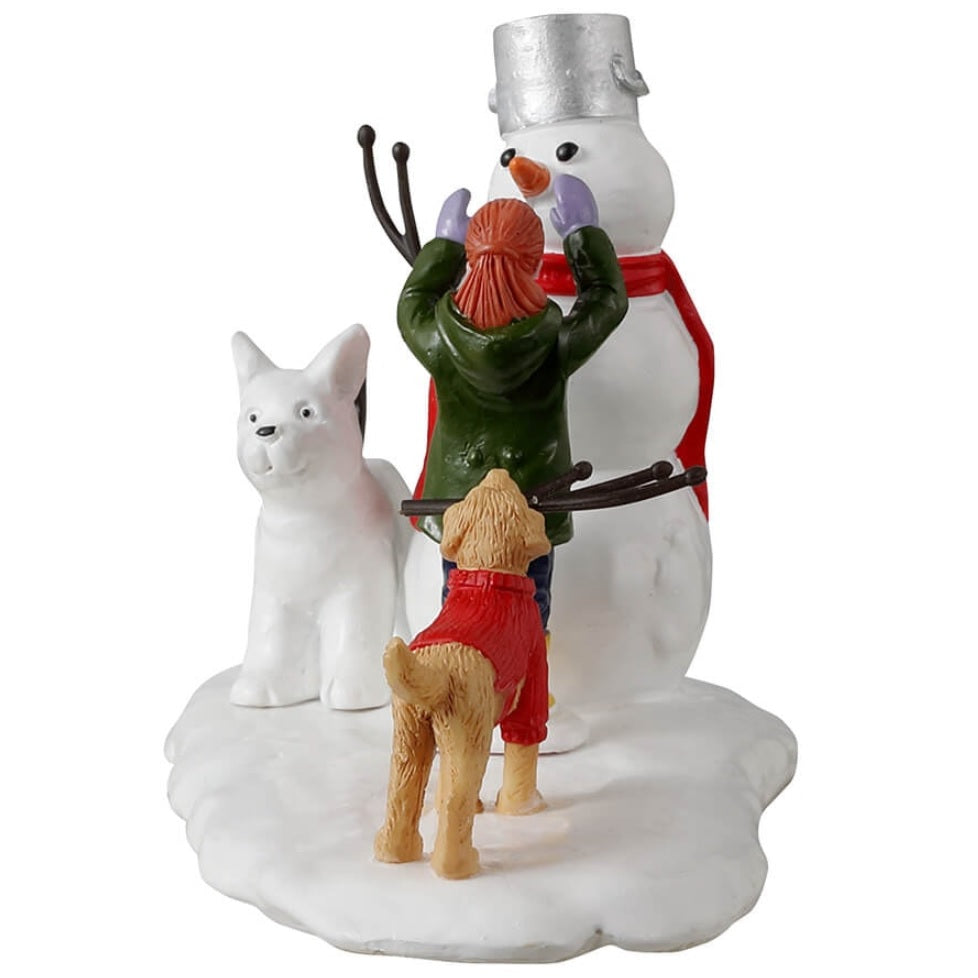 Resin village accent for a Lemax display. Designed to look like a young girl putting the finishing touches on a snowman. There's a dog holding a twig, trying to help. There's a dog made out of snow standing next to the snowman.