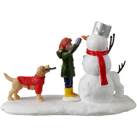 Resin village accent for a Lemax display. Designed to look like a young girl putting the finishing touches on a snowman. There's a dog holding a twig, trying to help. There's a dog made out of snow standing next to the snowman.