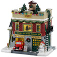 Porcelain lighted building for a Lemax display. Designed to look like a fire house decorated for Christmas. There are decorated trees and multi-colored lights on the roof. There are ladders on both sides of the building. In the window, you can see a decorated tree inside. There's a red firetruck parked in the garage and a snowman on the sidewalk.