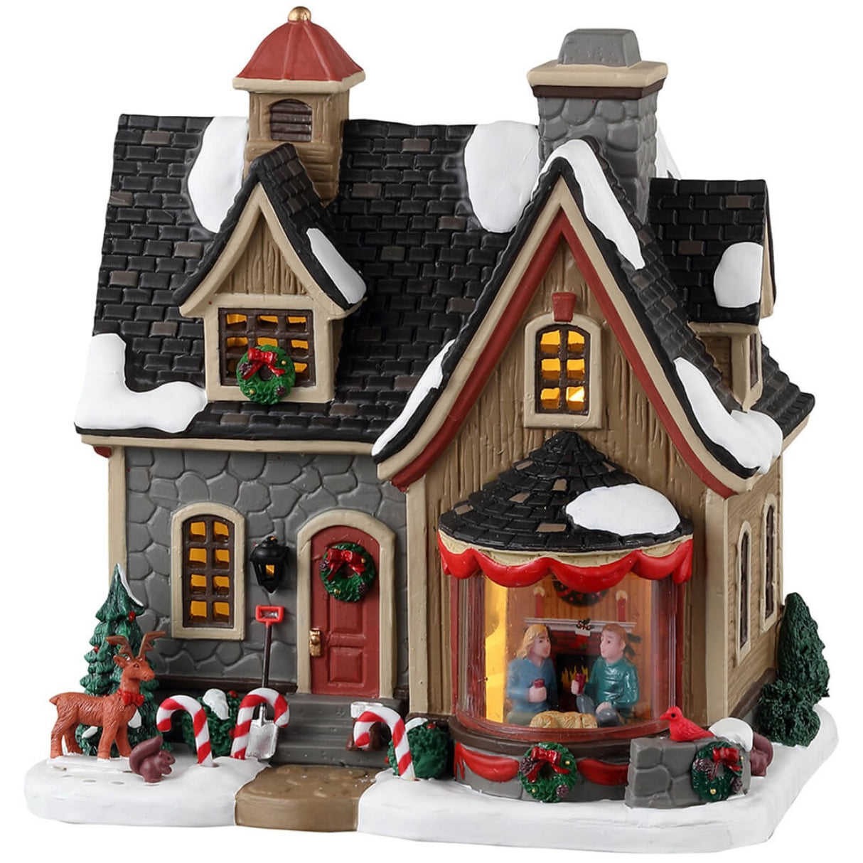Porcelain lighted building for a Lemax display. Designed to look like a cute home decorated for Christmas. There's snow on the roof and on the sidewalk. There are wreaths, red ribbons and candy cane accents. There's a reindeer and a squirrel near the front door. In the window, you can see a couple relaxing near a fireplace.