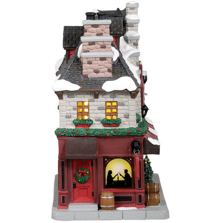 Porcelain lighted building for a Lemax display. Designed to look like a wine and chocolate tasting restaurant. There's a statue of a wine bottle, a wine glass and a piece of chocolate on the front. There are two decorated trees near the front door and a bunch of barrels on the sidewalk.