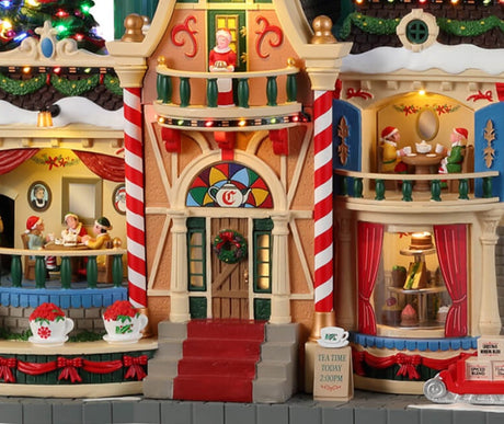Resin lighted building for a Lemax display. Designed to look like building decorated for Christmas. There are three large mug statues on the roof and a large red flag that reads "TEA WITH MRS. CLAUS."