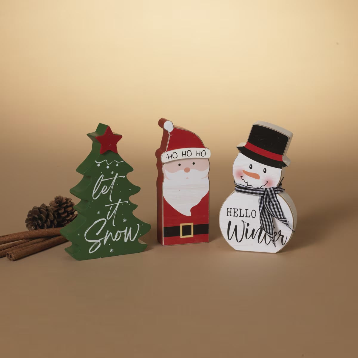 Christmas-themed shelf sitter decoration. One is shaped like a snowman wearing a top hat and reads "Hello Winter." One is shaped like a Christmas tree and reads "Let It Snow." One is shaped like Santa Claus and reads "Ho Ho Ho."