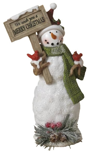 Decorative snowman figurine. This one is wearing a red, knit Santa hat and a green scarf and is holding a sign that reads "We wish you a MERRY CHRISTMAS."