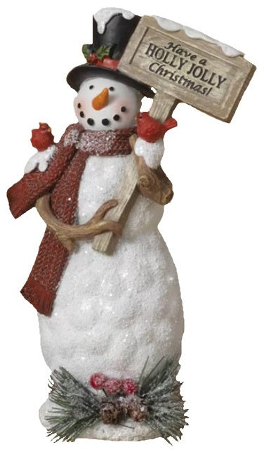 Decorative snowman figurine. This one is wearing a black top hat and a red scarf and is holding a sign that reads "Have a HOLLY JOLLY Christmas!"