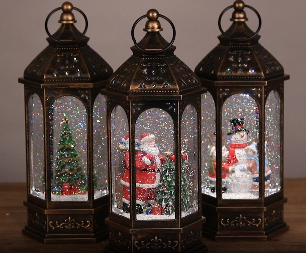Bronze lanterns with snow globe inside. One lantern features a snowman with two kids. One lantern features Santa with a tree. One lantern features a decorated tree with presents underneath. There's swirling glitter and lights inside.