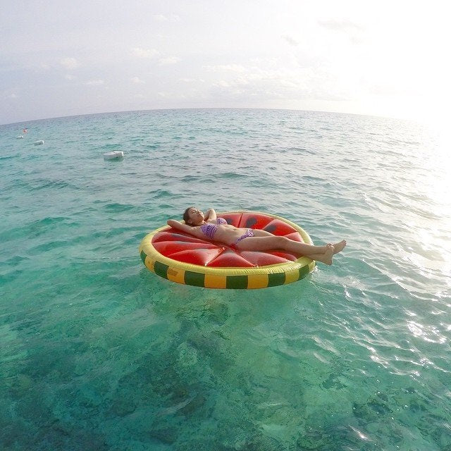 This is a lifestyle image showing a woman laying on the watermelon float while floating in the ocean.