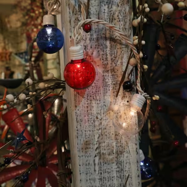 A string of red, white and blue globe lights wrapped around a white column.