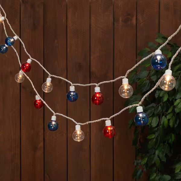 String of red, white and blue globe lights set against a brown fence.