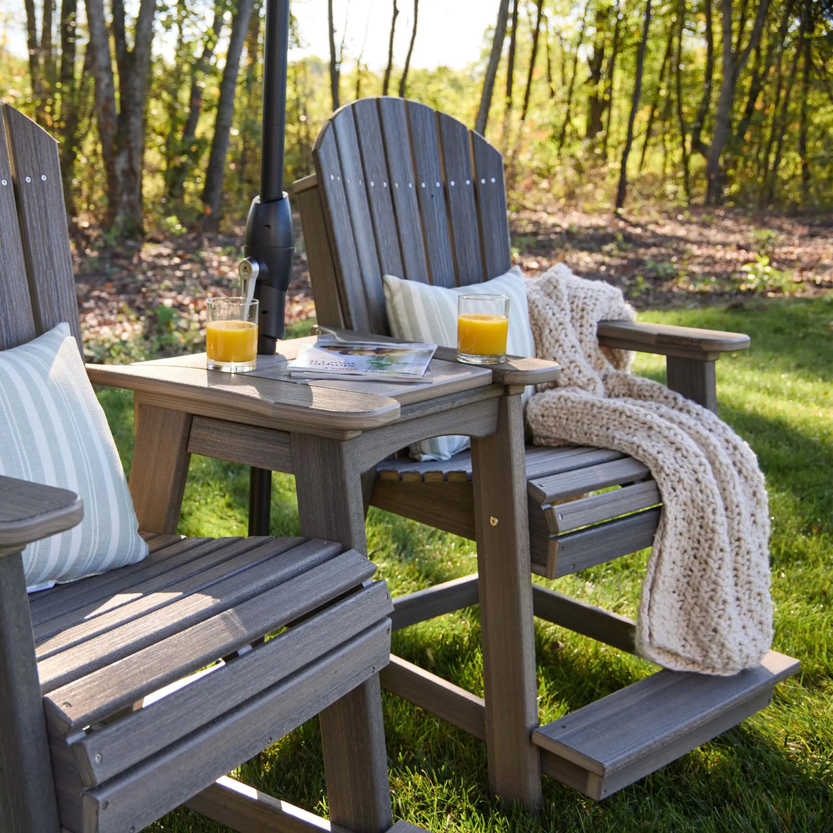 This is a lifestyle image showing two Weatherwood colored Balcony Adirondack Chairs in a grassy, sunny backyard.