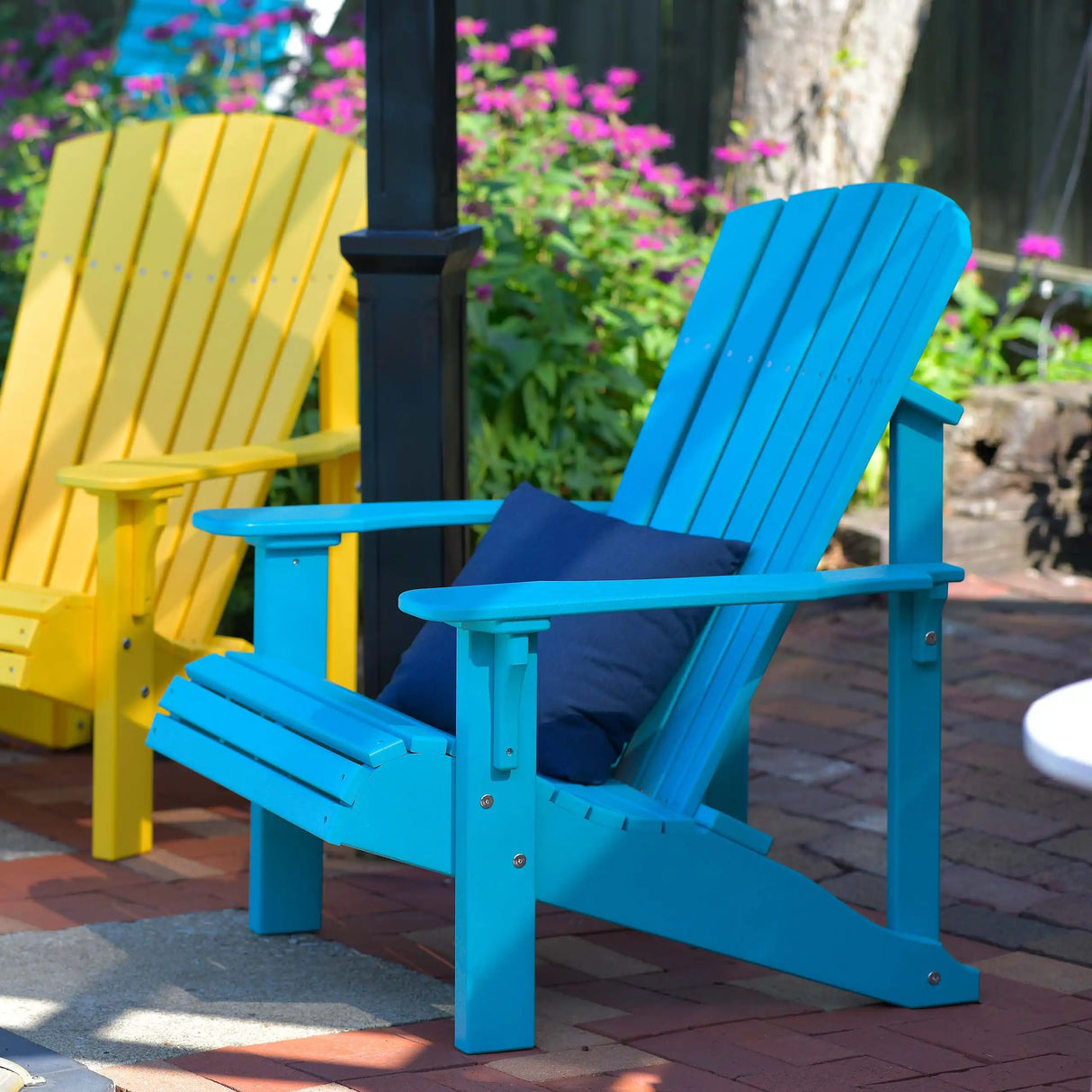 This is a lifestyle image showing two different colored Adirondack chairs on a brick patio. The chair on the left is Yellow and the chair on the right is Aruba Blue.