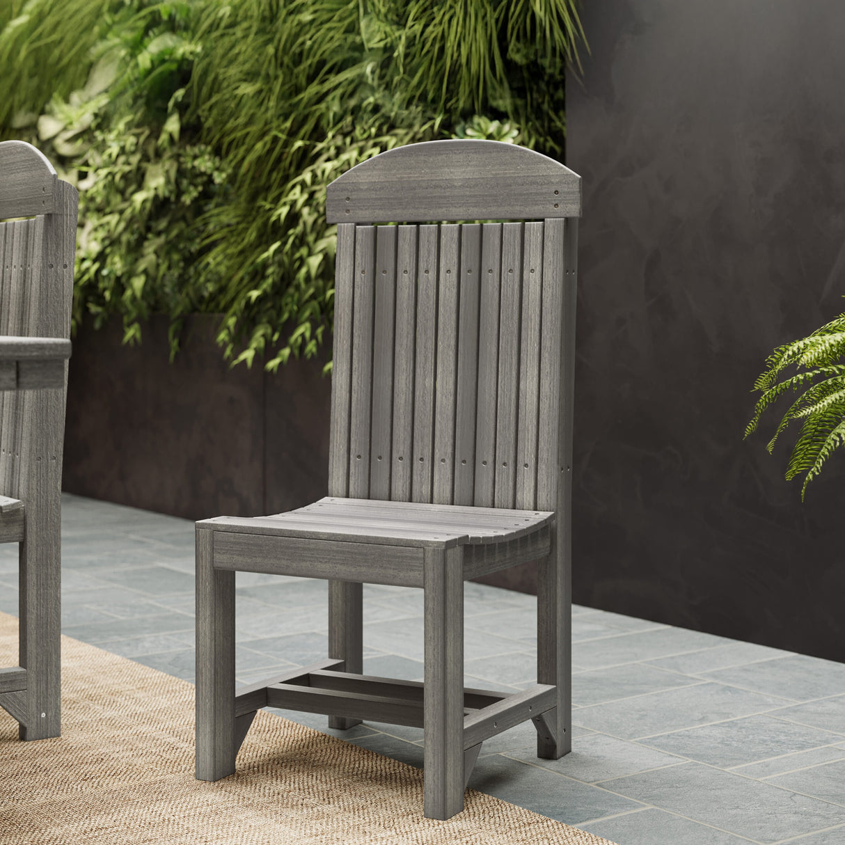 This is a lifestyle image showing the Coastal Gray colored Side Chair on a stone patio with greenery in the back.